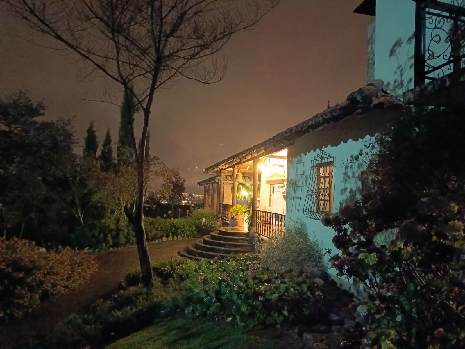 La Hostería Caballo Campana al anochecer: la casa de hacienda iluminada, su portal de columnas y el jardín.